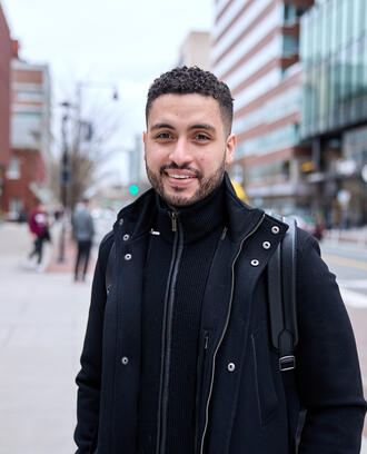 Mike Sanchez stands on a street in Cambridge and smiles at the camera